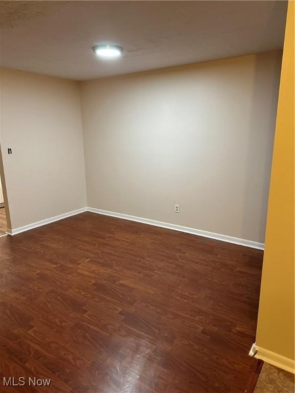 spare room featuring dark wood-style floors and baseboards