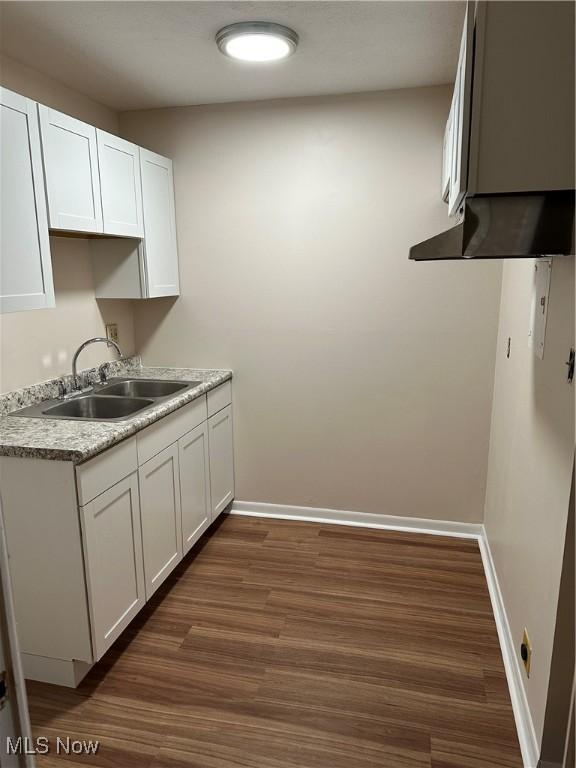 kitchen featuring dark wood-type flooring, white cabinetry, a sink, and baseboards