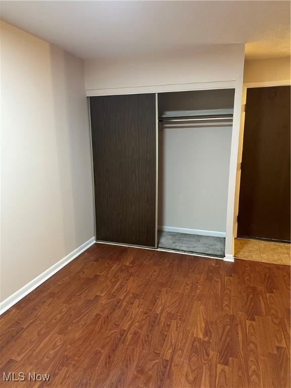 unfurnished bedroom with a closet, wood finished floors, and baseboards