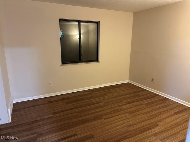 empty room featuring baseboards and dark wood-style flooring