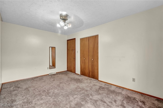 unfurnished bedroom with a textured ceiling, carpet floors, visible vents, baseboards, and a closet