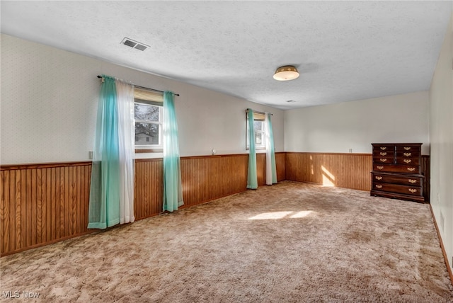 unfurnished room featuring wooden walls, visible vents, wainscoting, a textured ceiling, and carpet floors