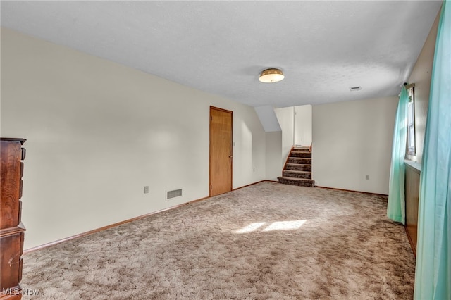 spare room with a textured ceiling, carpet flooring, visible vents, baseboards, and stairway