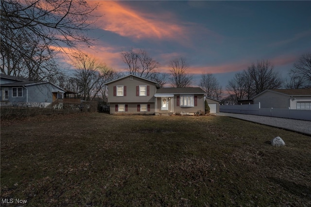 tri-level home with a garage, fence, driveway, and a lawn