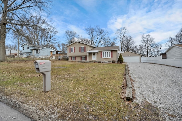 tri-level home with a garage, a front yard, fence, and an outdoor structure