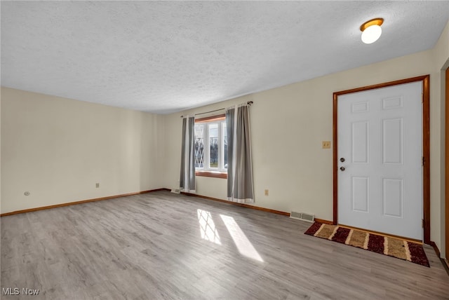 foyer featuring visible vents, a textured ceiling, baseboards, and wood finished floors