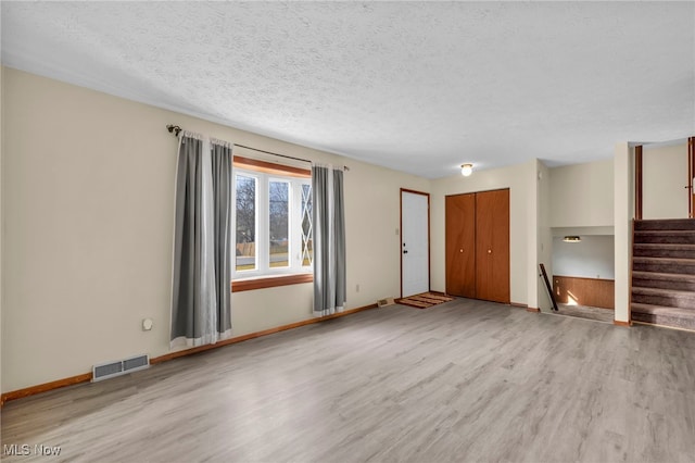 unfurnished living room featuring a textured ceiling, wood finished floors, visible vents, baseboards, and stairway