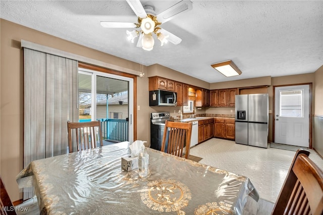 kitchen with a wealth of natural light, appliances with stainless steel finishes, brown cabinetry, and a textured ceiling