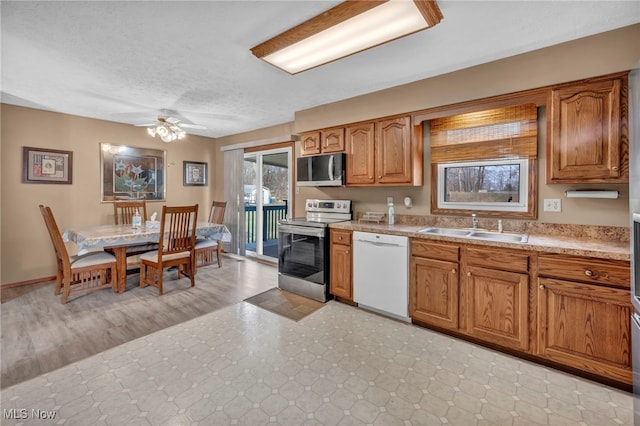 kitchen featuring brown cabinets, light floors, light countertops, appliances with stainless steel finishes, and a sink