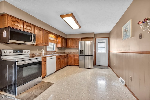 kitchen with visible vents, brown cabinetry, wainscoting, appliances with stainless steel finishes, and light countertops