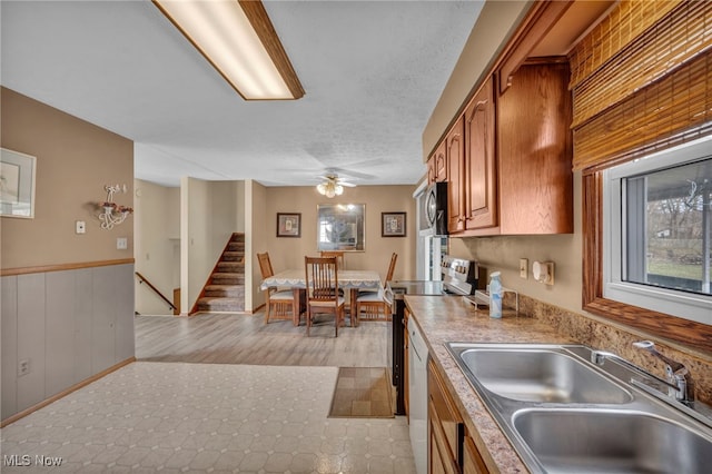 kitchen featuring ceiling fan, a wainscoted wall, stainless steel appliances, a sink, and brown cabinets