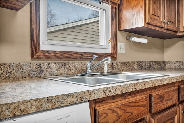 kitchen featuring light countertops, white dishwasher, a sink, and brown cabinets