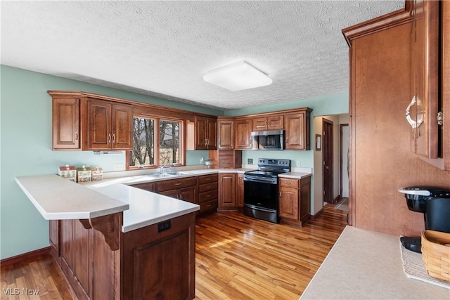 kitchen featuring light wood finished floors, a peninsula, stainless steel appliances, and a sink