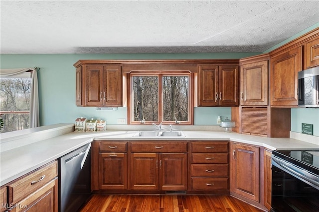 kitchen with brown cabinetry, dark wood finished floors, a sink, light countertops, and appliances with stainless steel finishes