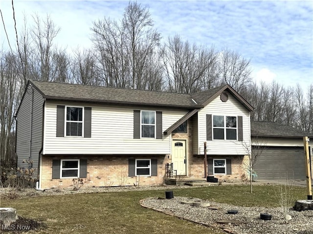 bi-level home featuring a garage, roof with shingles, a front yard, and brick siding