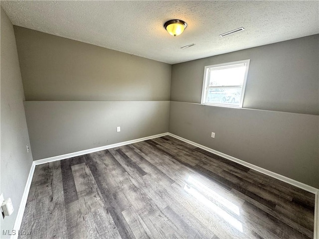 unfurnished room with baseboards, a textured ceiling, visible vents, and wood finished floors