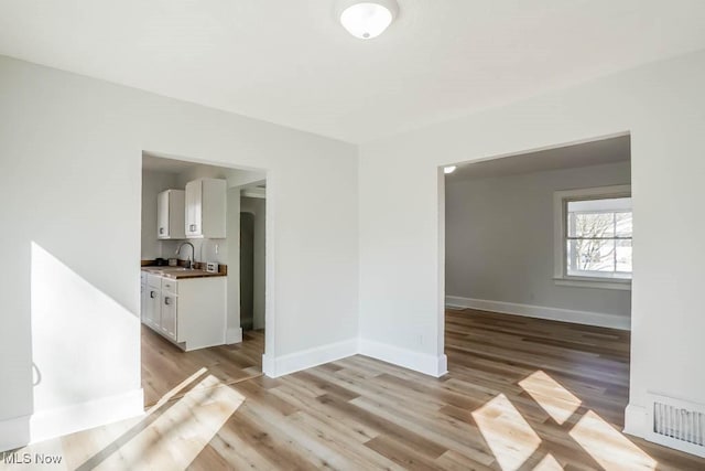 unfurnished dining area with light wood-type flooring, visible vents, a sink, and baseboards