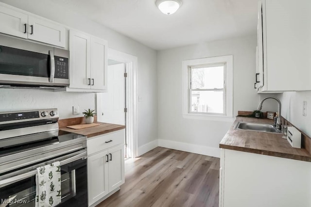 kitchen featuring stainless steel appliances, a sink, wood counters, white cabinetry, and light wood-style floors