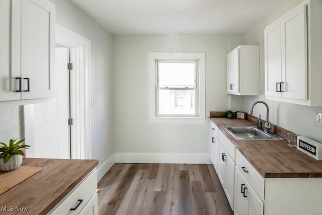 kitchen with white cabinets, baseboards, wooden counters, and a sink