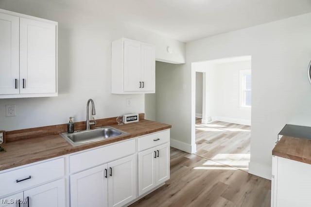 kitchen featuring light wood-style flooring, a sink, wood counters, baseboards, and white cabinets