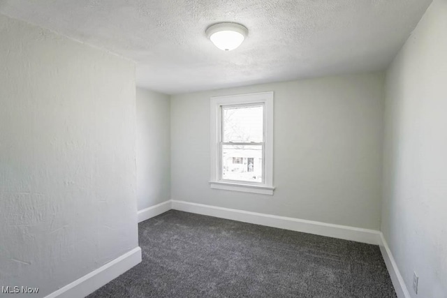 spare room with dark colored carpet, a textured ceiling, and baseboards