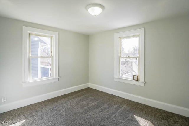 spare room featuring dark carpet and baseboards