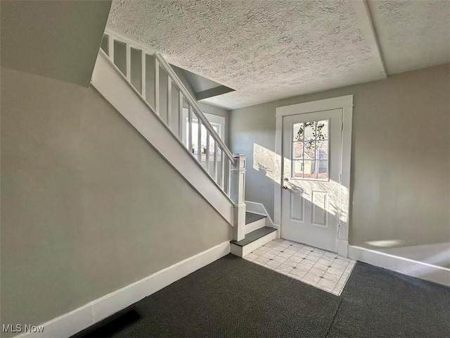 tiled foyer entrance with a textured ceiling, stairway, baseboards, and a healthy amount of sunlight