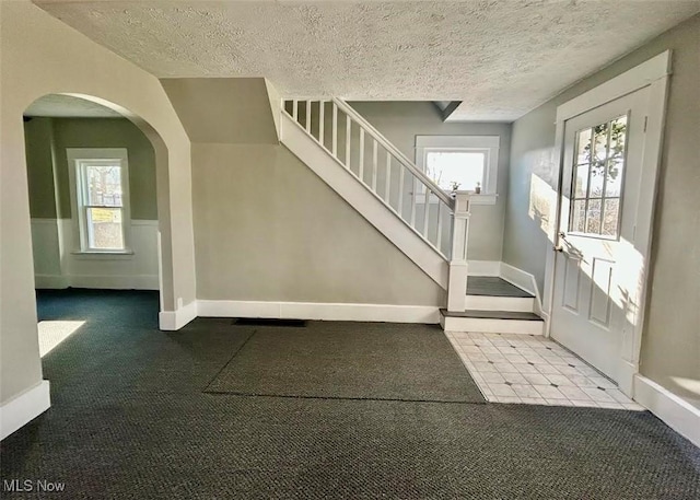 entrance foyer featuring carpet floors, arched walkways, a textured ceiling, and stairs