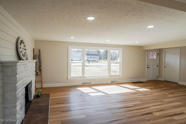 unfurnished living room with visible vents, light wood-style flooring, a textured ceiling, a fireplace, and recessed lighting