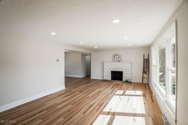 unfurnished living room featuring light wood-style floors, a fireplace with flush hearth, baseboards, and a textured ceiling