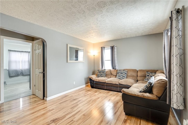 living area with light wood-type flooring, arched walkways, a textured ceiling, and baseboards