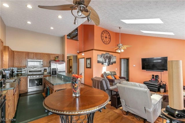 kitchen featuring a skylight, brown cabinets, stainless steel appliances, dark countertops, and a sink