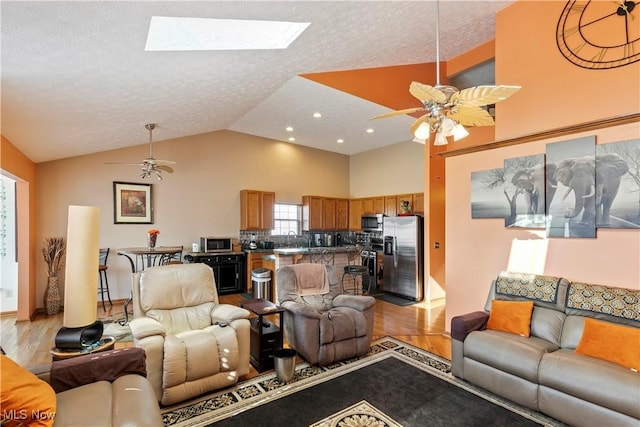 living room featuring a skylight, ceiling fan, light wood-style flooring, and a textured ceiling