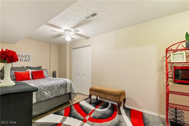 bedroom with a textured ceiling, carpet floors, visible vents, baseboards, and a ceiling fan