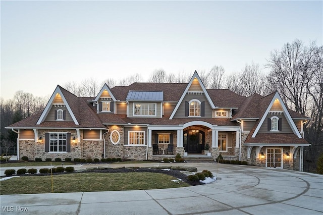 shingle-style home with stone siding, curved driveway, and a front lawn