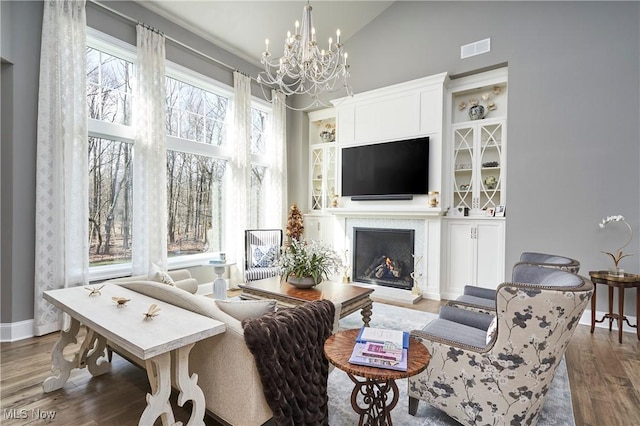 living area featuring high vaulted ceiling, a notable chandelier, wood finished floors, visible vents, and a lit fireplace