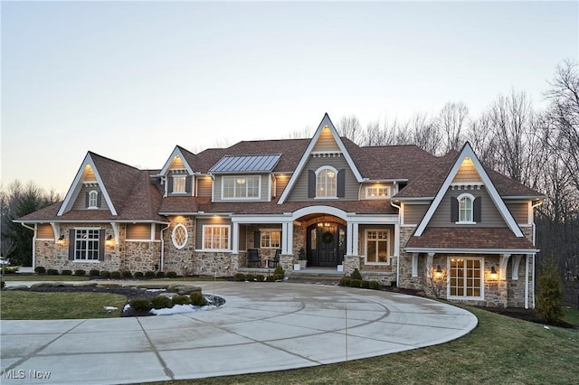 shingle-style home featuring stone siding, curved driveway, and a front lawn