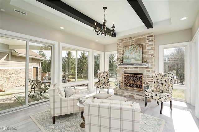 sunroom / solarium featuring a notable chandelier, visible vents, beam ceiling, and a stone fireplace