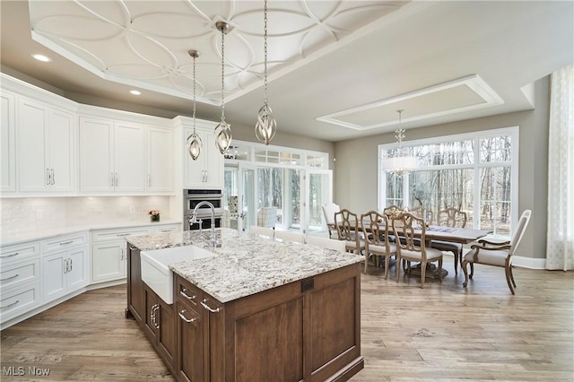 kitchen with white cabinets, a raised ceiling, stainless steel double oven, light wood-type flooring, and a sink