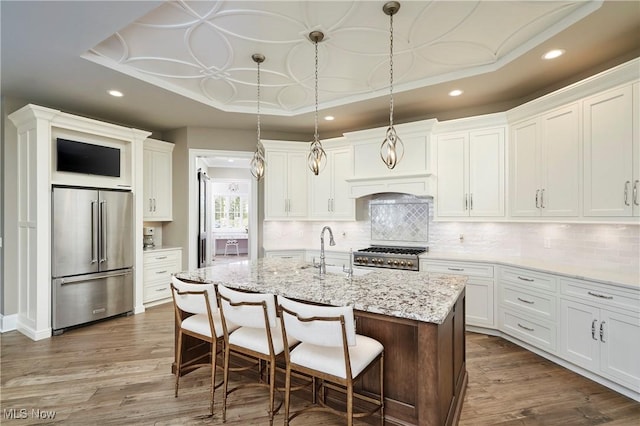 kitchen with high end refrigerator, range, dark wood-style floors, a tray ceiling, and a sink