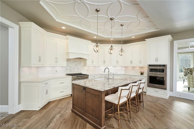 kitchen featuring a breakfast bar, a raised ceiling, double oven, a sink, and wood finished floors