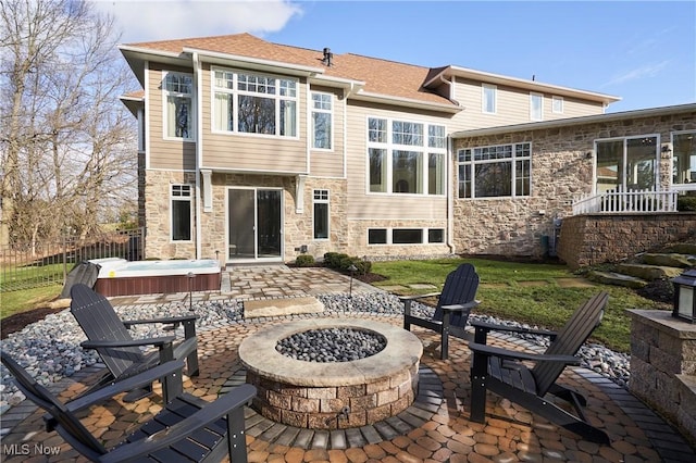 rear view of property with a patio, an outdoor fire pit, fence, stone siding, and a hot tub