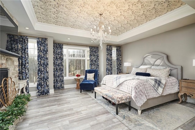 bedroom with ornamental molding, a raised ceiling, a fireplace, and wood finished floors