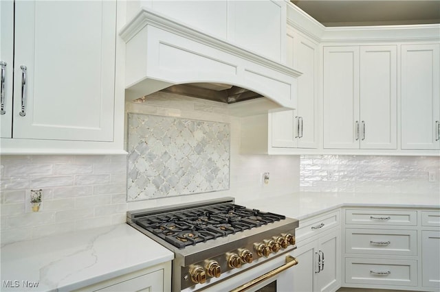 kitchen featuring gas stove, white cabinets, custom range hood, and decorative backsplash