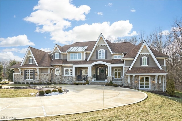 view of front facade featuring driveway, stone siding, and a front lawn