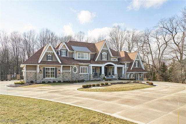 shingle-style home with driveway, a front lawn, and stone siding