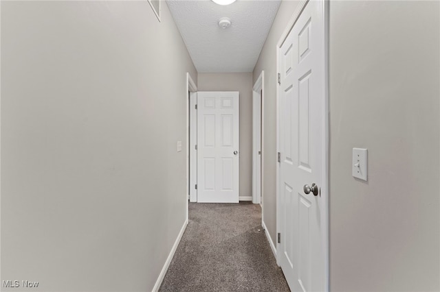 hallway featuring baseboards, dark carpet, and a textured ceiling