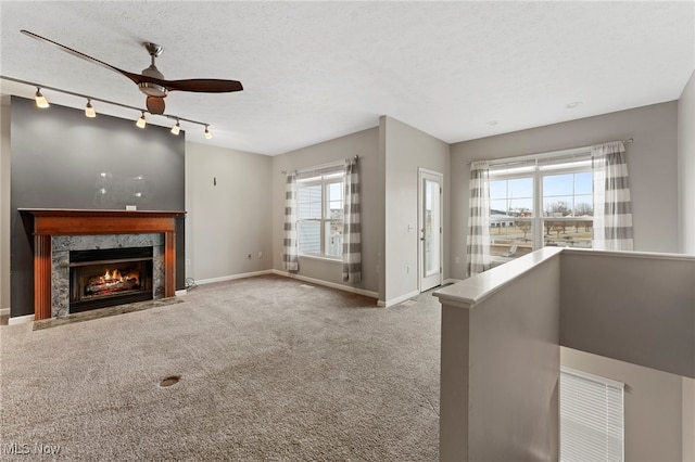 unfurnished living room featuring a textured ceiling, ceiling fan, carpet floors, a fireplace, and baseboards