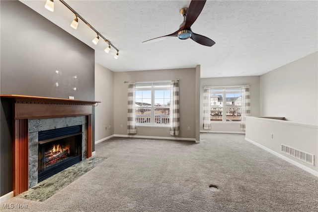 unfurnished living room featuring carpet floors, visible vents, a premium fireplace, a textured ceiling, and baseboards