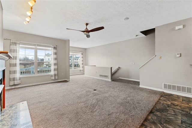 unfurnished living room with a textured ceiling, carpet flooring, visible vents, and baseboards